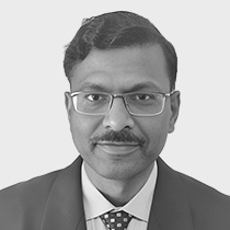 Professional headshot of a man wearing glasses, a dark suit, and a tie, against a light neutral background.